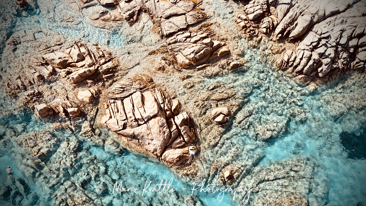 Aerial view of granite rocks meeting turquoise water